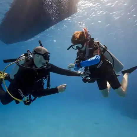 A SCUBA Diving instructor checks with a junior diver as they descend underneath a boat in clear water