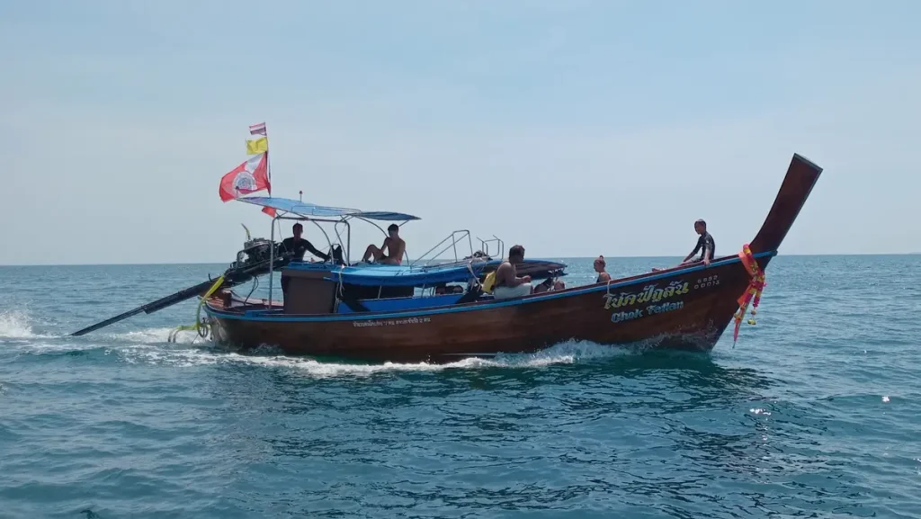 a wooden longtail boat under power on a calm sea on a sunny day with scuba divers onboard