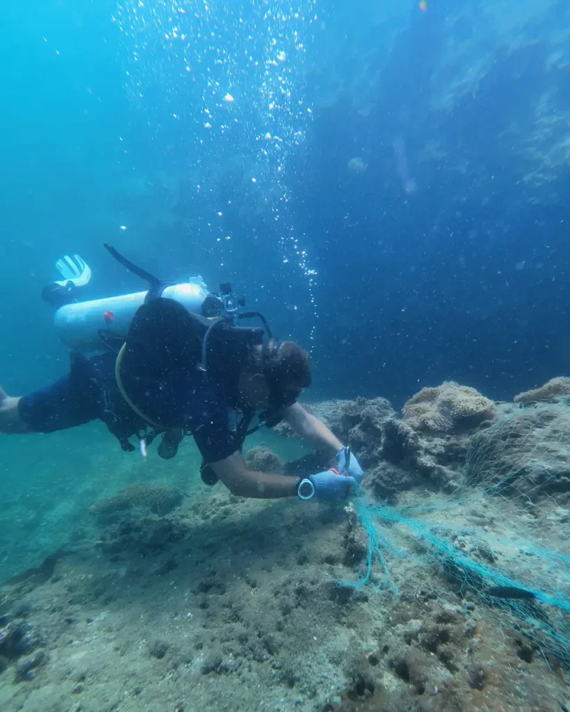 a diver works to cut a discarded fishing net off a coral reef