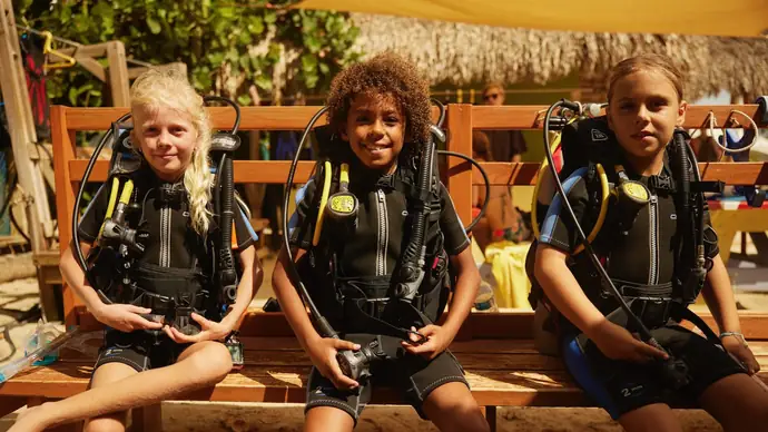 three children sitting on a bench wearing scuba gear, ready for their first lesson