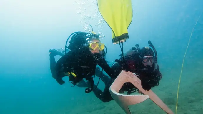 two scuba divers in mid water have used a large yellow lift bag to help float an anchor so they can manouvere it underwater. part of the search and recovery course.