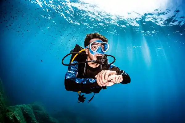a calm scuba diver approaches with clear water and sunsplash on the surface above and rocky coral reef below