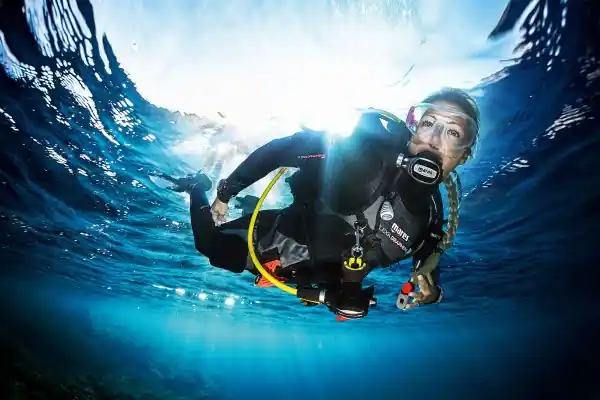 a female diver begins here descent from the clear blue ocean surface