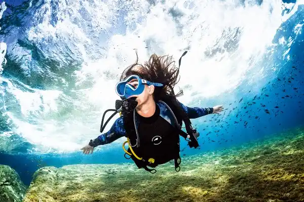 a female scuba diver descends from the clear blue ocean surface, she looks happy with arms outstretched, looking to her right as she begins a new dive