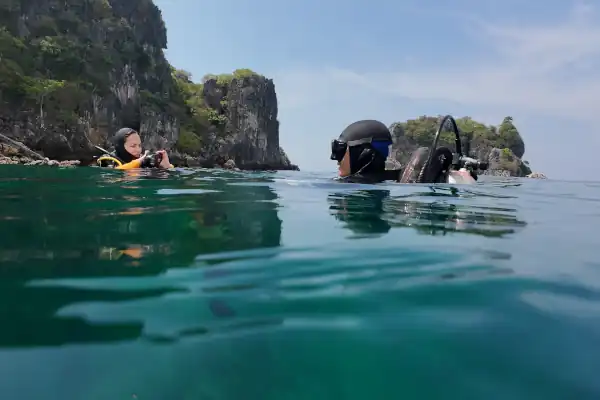 Two divers at the surace of a clam sea. Island in the background. Preparing to descend.